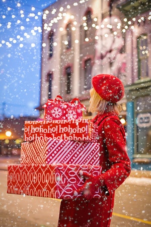 Photo of woman in red coat holding wrapped gifts in the snow
