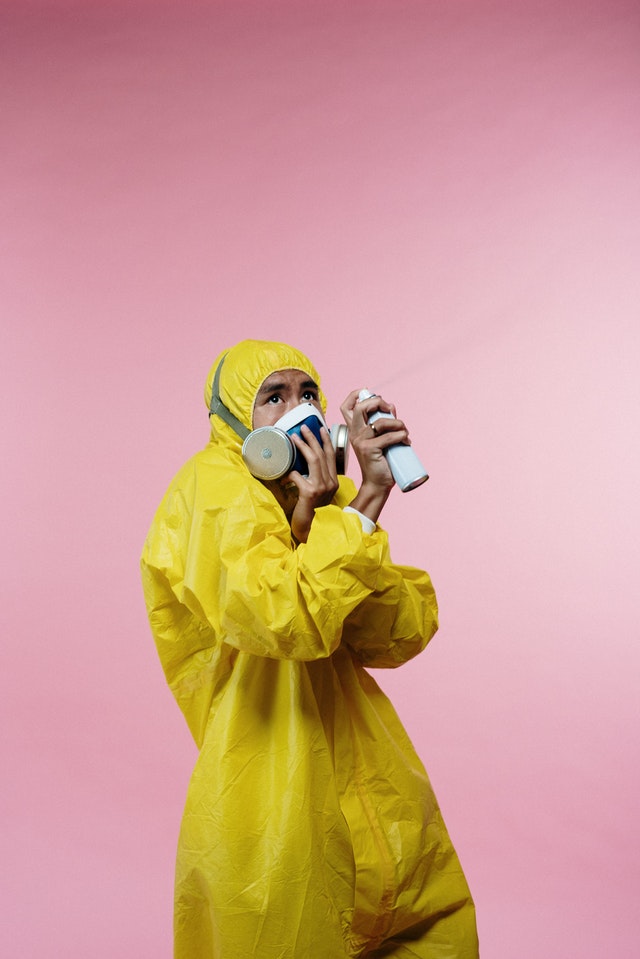 Man in yellow suit and face mask spraying disinfectant
