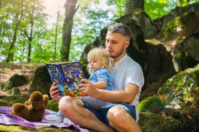 Dad reading to small child on picnic blanket