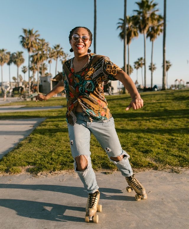 Happy woman in colorful shirt and ripped jeans skating 