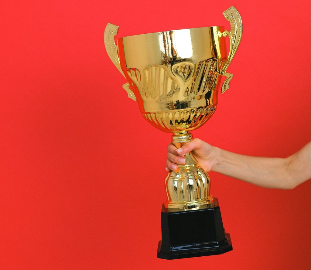 Arm holding large, gold trophy in front of red background